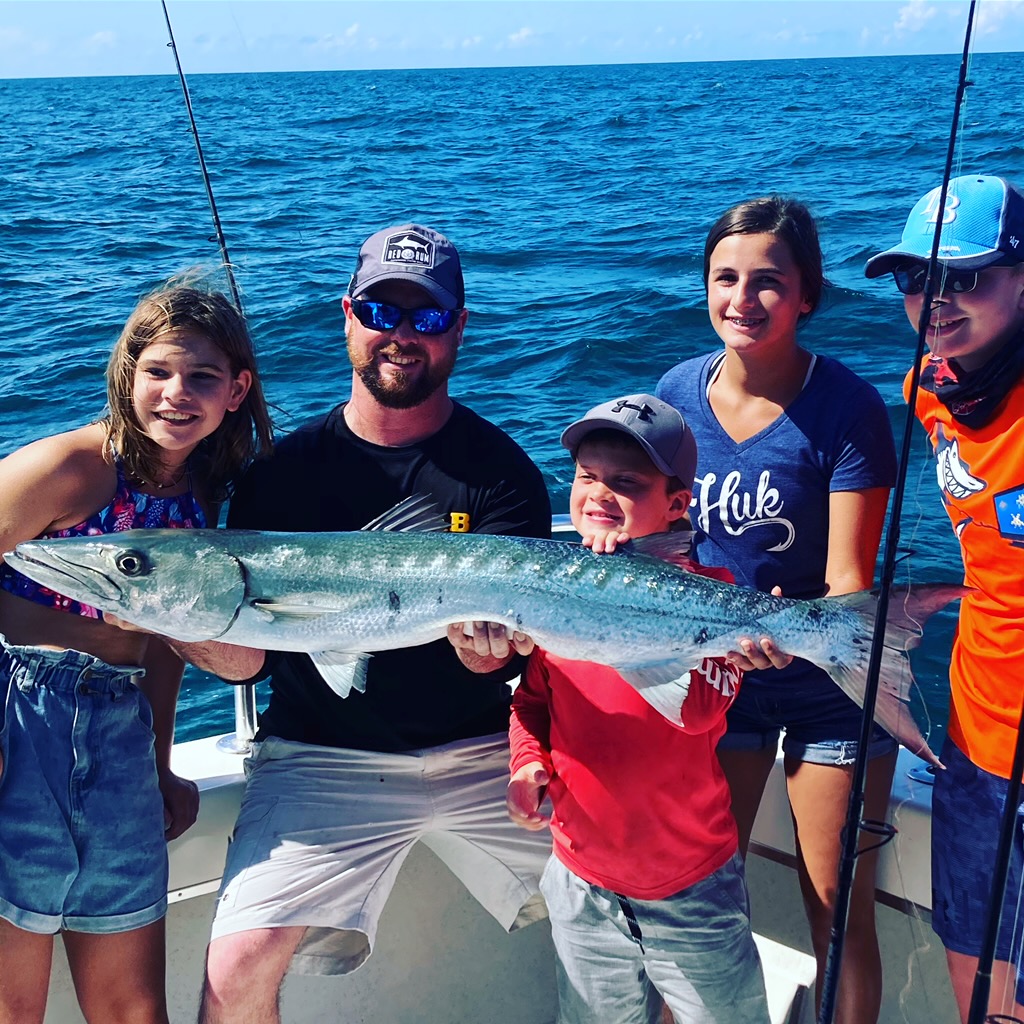 Captain Bobby of A and B Charters, along with anglers holding a barracuda